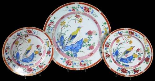 A pair of famille rose porcelain plates, decorated with exotic birds within a landscape, with inner border of pink ground and lotus flowers, scattered flower spray with an outer border of an orange ground and gilt bands, interestingly decorated with var