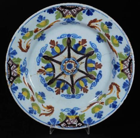 An 18thC English Delft pottery plate, of circular form, polychrome decorated with flowers in a geometric centre, predominately in blue, yellow and green, probably Vauxhall, 22cm Dia. (AF)