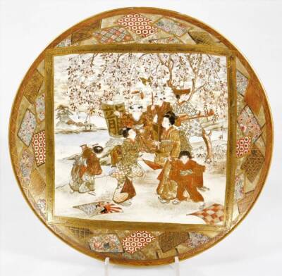 A 19thC Japanese Meiji period Satsuma pottery plate, of circular form, set with many geisha and children before a blossom tree, with an outer geometric banding, predominately in green and blue with gilt highlights, seal mark and remnants of collector's la