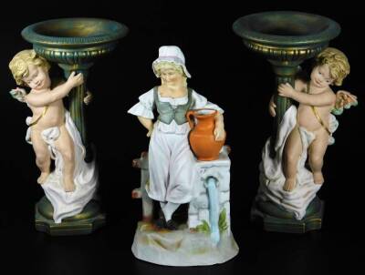 A continental bisque porcelain figure of a girl, aside ewer and bell, with a gate in the distance, on a naturalistic base, polychrome decorated predominately in orange, blue and green, 28cm H, and a pair of bisque porcelain cherub stands. (3)
