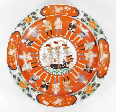 A Japanese Edo period Dutch export porcelain charger, centred with a ship surrounded by figures smoking pipes in 17thC dress, with an outer floral border broken by further panels on orange and blue ground, with gilt highlights, further decoration and sagg