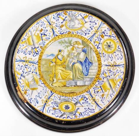 An Italian Maiolica wall plaque, of circular form, with a religious scene of Virgin and Child and an outer border decorated with swords, scrolls and lines predominately in yellow and green, 34cm Dia.