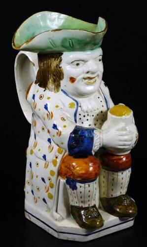 An early 19thC Prattware Toby jug, the toper sat in floral jacket picked out in yellow, holding a jug, aside pipe, with green hat, orange breeches and brown shoes, 24cm H.