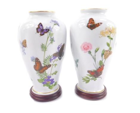 A pair of Franklin Porcelain vases, decorated with butterflies, designed by John Wilkinson, comprising The Meadowland Butterfly vase, and The Country Garden Butterfly vase, raised on turned wooden stands, 31cm H.