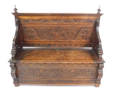 A Victorian oak settle, the back carved with a shield flanked by griffins' heads, scrolling leaves and flowers, with scrolling arms carved with lion and dolphins' heads, the base foliate and floral carved, raised on block feet, 118cm H, 137cm W, 50cm D.