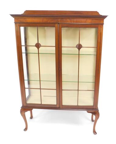 An early 20thC mahogany display cabinet, the outswept pediment over a pair of glazed doors enclosing two glass shelves, raised on cabriole legs, with shell carved knees, 160cm H, 107cm W, 34cm D.