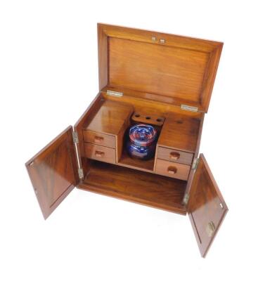 An early 20thC walnut smoker's cabinet, with a hinged lid and two doors, opening to reveal a central recess, holding a stoneware tobacco jar, backed by a triple pipe holder flanked by four drawers above a recess raised on a stepped plinth base, 33cm H, 43 - 2