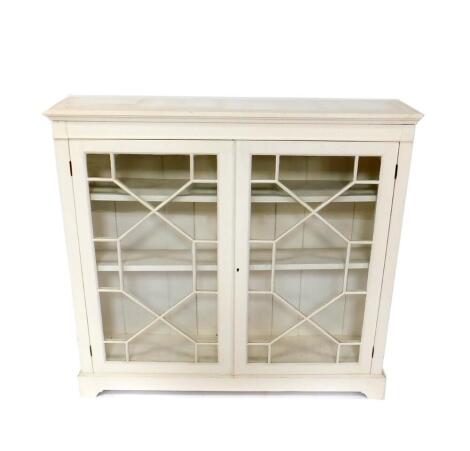 A Maple & Company early 20thC bookcase, later cream painted, the outswept cornice, over two astragal glazed doors, enclosing two shelves, raised on bracket feet, 113cm H, 121cm W, 28cm D.