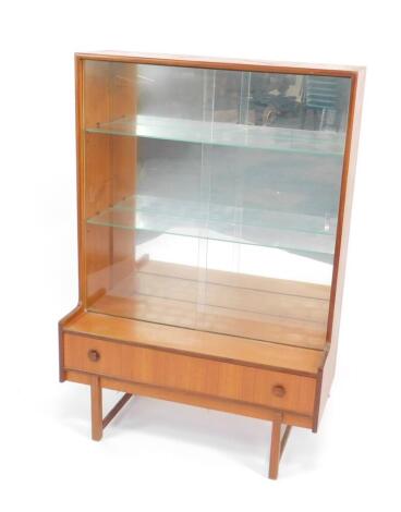 A Turnidge of London 1960's teak bookcase, with two glass doors, opening to reveal a mirror backed interior, with two glass shelves, over a single frieze drawer, raised on square legs. 132cm H, 91cm W, 40.5cm D.