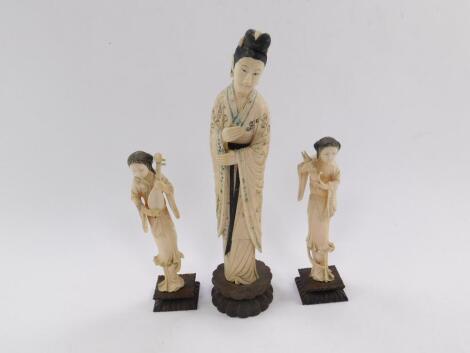 A Chinese early 20thC ivory okomono of a standing lady, with black and blue ink decoration, raised on a wooden circular base, 29cm H, together with a pair of ivory figures modelled as female musicians, raised on square wooden bases, 19cm H. (3)