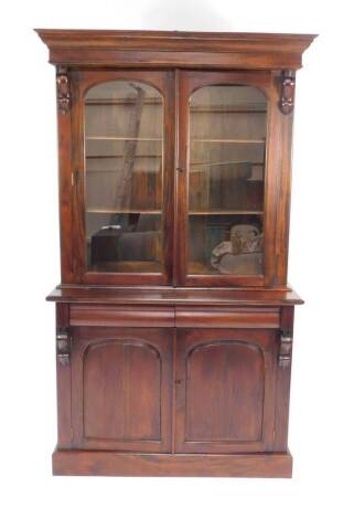 A Victorian style hardwood cupboard bookcase, the outswept pediment over two glazed doors enclosing two shelves, over a pair of cushion drawers above panelled doors, raised on a plinth base, 204cm H, 122cm W, 45cm D.