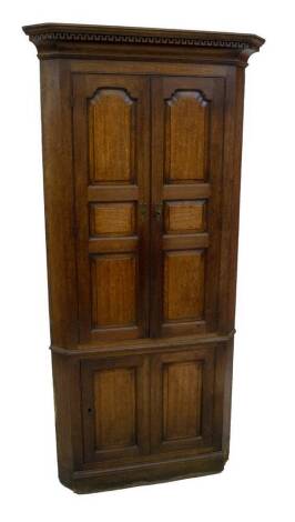 A George III oak freestanding corner cupboard, having Greek key carved and moulded cornice, over two long doors, with three shaped and fielded panels to each door, revealing shaped shelves over a single door base and plinth, 209cm H, 95cm W across the can