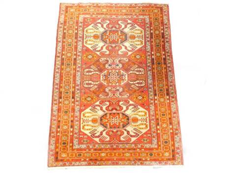 A Caucasian rug, with Dagestan-style geometric panels, woven with a hot orange centred triple border of the region,  200cm x 140cm