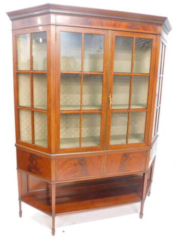 An Edwardian mahogany and satinwood cross banded display cabinet, the moulded cornice with a Greek key frieze, above two astragal glazed doors, flanked by canted glazed sides, above two central doors, on square tapering legs with under tier and spade feet