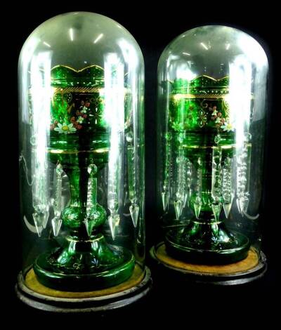 A pair of Victorian green glass lustres, each decorated in coloured enamels with flowers, leaves etc., within gilt borders, each in a glass dome with ebonised base 50cm H.