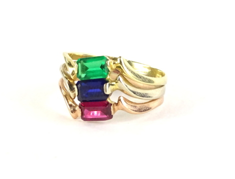 A three row dress ring, set with three baguette cut stones, emerald, ruby and sapphire, with wave design borders, yellow metal, marked 585, ring size P½, 3.4g all in.