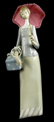 A Lladro porcelain figurine, modelled in the form of a lady with a lacy parasol, carrying a box or basket, 35cm H.