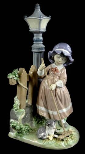 A Lladro porcelain figure group, depicting a girl raking leaves beside a lamp post, with a cat, 33cm H.