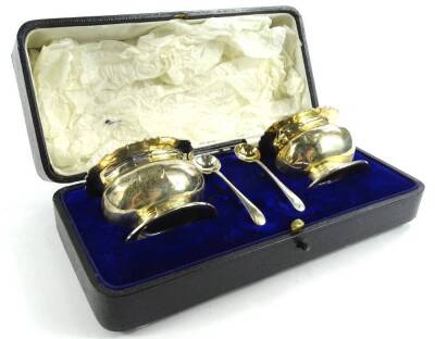 A George V silver open salt set, comprising two bombe shaped salts with repousse decorated leaf and berry tops, on oval feet, and associated two spoons, Chester 1911, etc., 2 ½ oz, (cased).