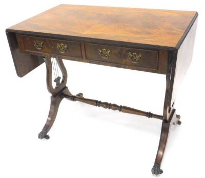 A mahogany sofa table in Regency style, the rectangular quarter veneered top with a cross banded and ebony strung border, above two frieze drawers, opposing two false drawers on liar shaped supports, with turned stretcher, splayed legs and brass paw feet,