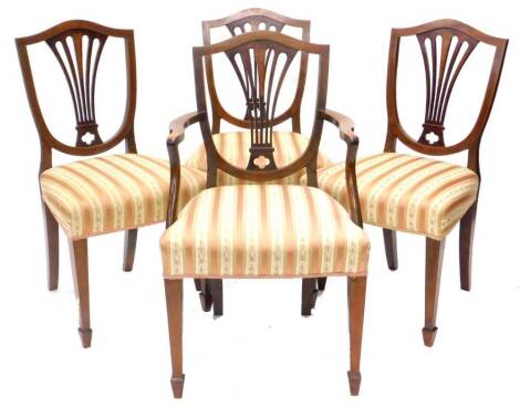 A set of four Edwardian mahogany chequer banded and boxwood strung dining chairs, each with a pierced splat inlaid in satinwood with bell flowers, a padded seat on square tapering legs with spade feet, one with arms.