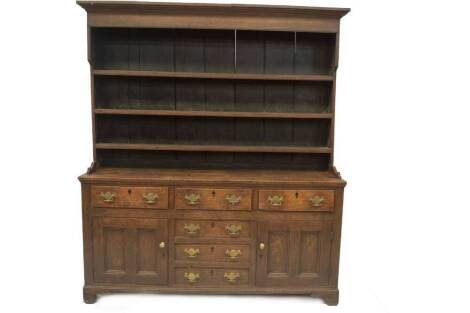 An 18thC oak dresser with plate rack, having moulded cornice, boarded back and three channelled shelves to the top, the base having three frieze drawers over three centre doors flanked by two double fielded moulded panel doors, with ebony escutcheons, bra