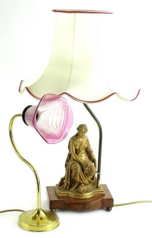 Two decorative table lamps, one example mounted with a spelter figure with a tapering shade, the other a brass base and a cranberry tinted shade with trail decoration.