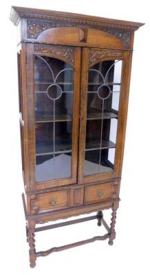 A carved oak display cabinet, with a moulded cornice above two leaded glazed doors, and frieze drawer, on spirally turned supports, 76cm W.