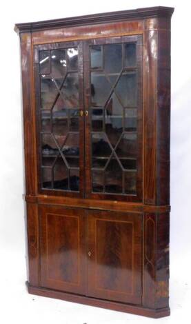 A George III mahogany standing corner cabinet, the inverted breakfront cornice above a frieze inlaid with patera and a dogtooth and satinwood crossband, the two astragal glazed doors enclosing a fitted interior, above two flat panelled doors, on a plinth 