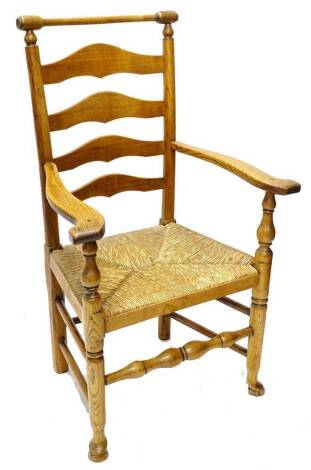 A 19thC ash ladder back chair, with a turned rail, shaped arms and rush seat with turned tapering legs and pad feet.