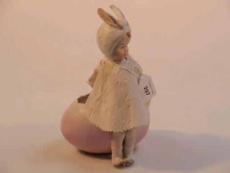 An early 20thC Bisque piano baby modelled as an Easter bunny and egg