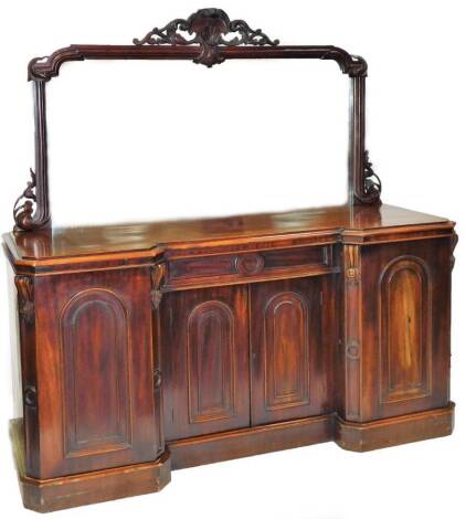 A Victorian mahogany inverted breakfront mirror back sideboard, the shaped glass surmounted by a carved scroll and shell motif, with an arrangement of further scrolls to each corner, above a canted top and four cupboards, each with arched panelled doors o