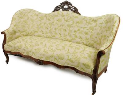 A Victorian walnut serpentine sofa, surmounted by an arrangement of carved scrolls and flowerheads, upholstered in green and cream button back floral material, with a carved scroll apron on cabriole legs terminating in castors, 176cm W.