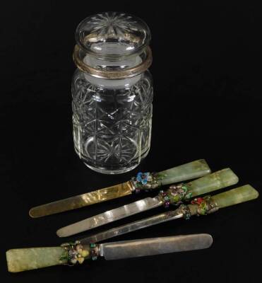 A harlequin set of five Edwardian silver and jade entree knives, each with elaborate turned floral handles, with claw set stone collars, three with silver blades, Sheffield 1902, 18cm W, and a cut glass jar with silver collar. (5)