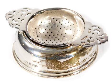 An Elizabeth II silver tea strainer on stand, with two pierced handles and centre, on a plain circular base, Birmingham 1958, 2½oz, 10cm W. (2)