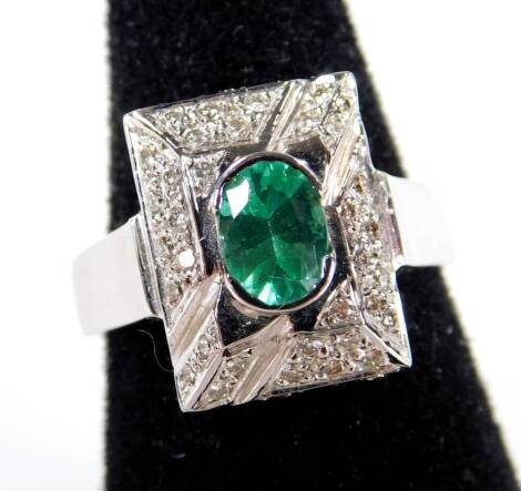 An emerald and diamond Art Deco style dress ring, with oval cut tension set emerald, 6mm x 4.8mm, with pave set diamonds to ring head, 1.4cm high, on plain band, white metal stamped 750, ring size O, 8.6g all in.