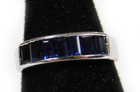 A sapphire half hoop eternity ring, set with seven baguette cut sapphire stones, in a rub over setting, white metal stamped 585, ring size N, 3.2g all in.