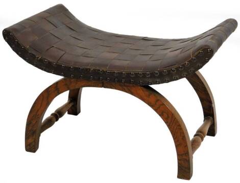 A Glastonbury style stool, with C shaped leather top on curved legs, joined by turned stretchers, 39cm H, 61cm W, 35cm D.