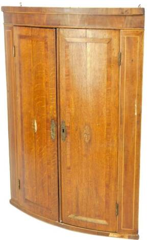 A George III oak and mahogany hanging corner cupboard, with oval shell patera to each door, 103cm H, 76cm W, 42cm D.