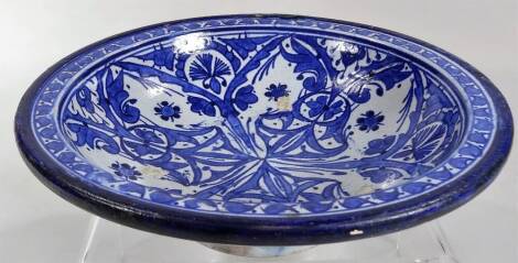 A tin glazed earthenware blue and white pottery bowl, of circular form, decorated with a floral and geometric pattern with an outer floral rim on circular foot, marked beneath, 25cm Dia.