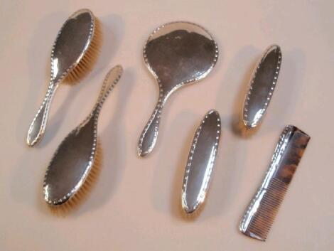 A silver-backed dressing table set comprising hand mirror