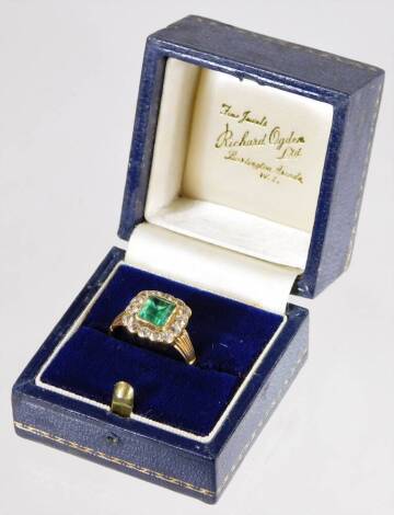 An emerald and diamond ring, with rectangular cut emerald, surrounded by old cut diamonds, each in rub over setting, the emerald 5mm x 6.4mm x 2mm, approx 0.45cts, surrounded by fourteen diamonds, totalling approx 0.14cts, with fluted fan design shoulders