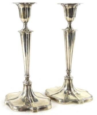 A pair of George V silver candlesticks, in neo-classical style, each with reeded shaped borders, a tapering column and a domed foot, loaded, London 1910, 29cm H.