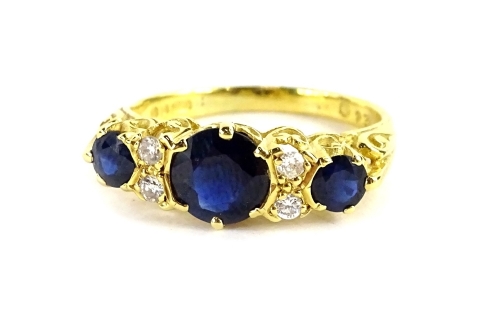 An 18ct gold gypsy ring, set with three sapphires and four tiny diamonds, the round brilliant cut sapphires with central stone flanked by two smaller stones, with two tiny diamonds to each side, in claw setting, with scroll design shoulders, ring size M½,