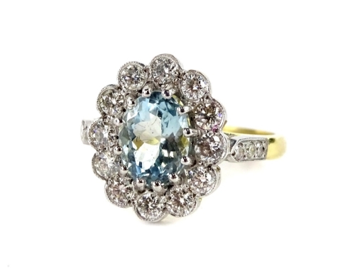 An 18ct gold and platinum aquamarine and diamond daisy ring, with oval cut aquamarine, in claw setting, 6.2mm x 8.4mm x 4.8mm, surrounded by twelve round brilliant cut diamonds, in rub over setting, each approx 0.05cts, with three tiny diamond set shoulde