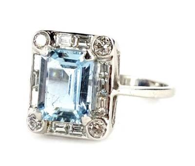 An aquamarine and diamond ring, in the Art Deco style, with central rectangular cut aquamarine, 8.8mm x 6.6mm x 4.2mm, with four round brilliant cut diamond corners, in rub over setting, with two/three design baguette cut diamond sides, white metal band,