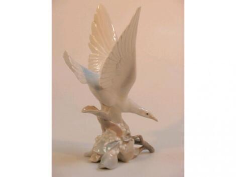 A Lladro figure of a seagull alighting on a rocky crag with foliage