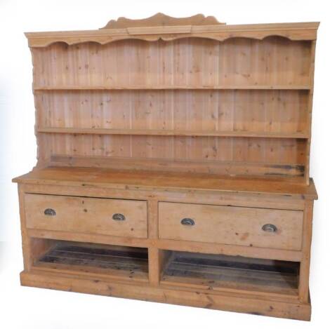 A pine dresser, the raised back with two shelves for plates, the base with two deep drawers and above two recesses, on a plinth, adapted from possibly from a 19thC shop counter unit, 198cm H, 213cm W.