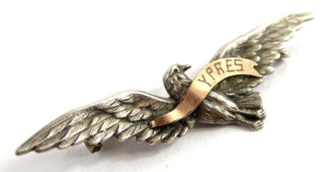 A white metal and rose coloured metal pin badge, depicting a bird in flight with banner emblazoned Ypres, 6cm W.