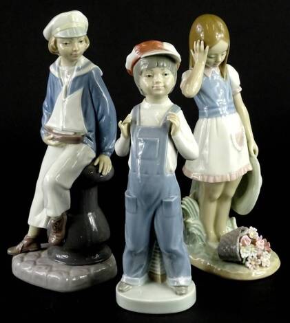 Three Lladro porcelain figurines, boy wearing cap with an accordion, a sailor, and a young girl with flowers.